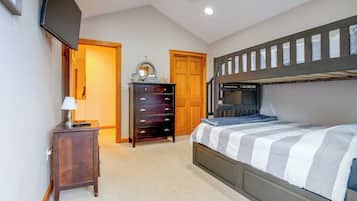 A bedroom with a bunk bed, a dresser, a lamp, and a door leading to another room.