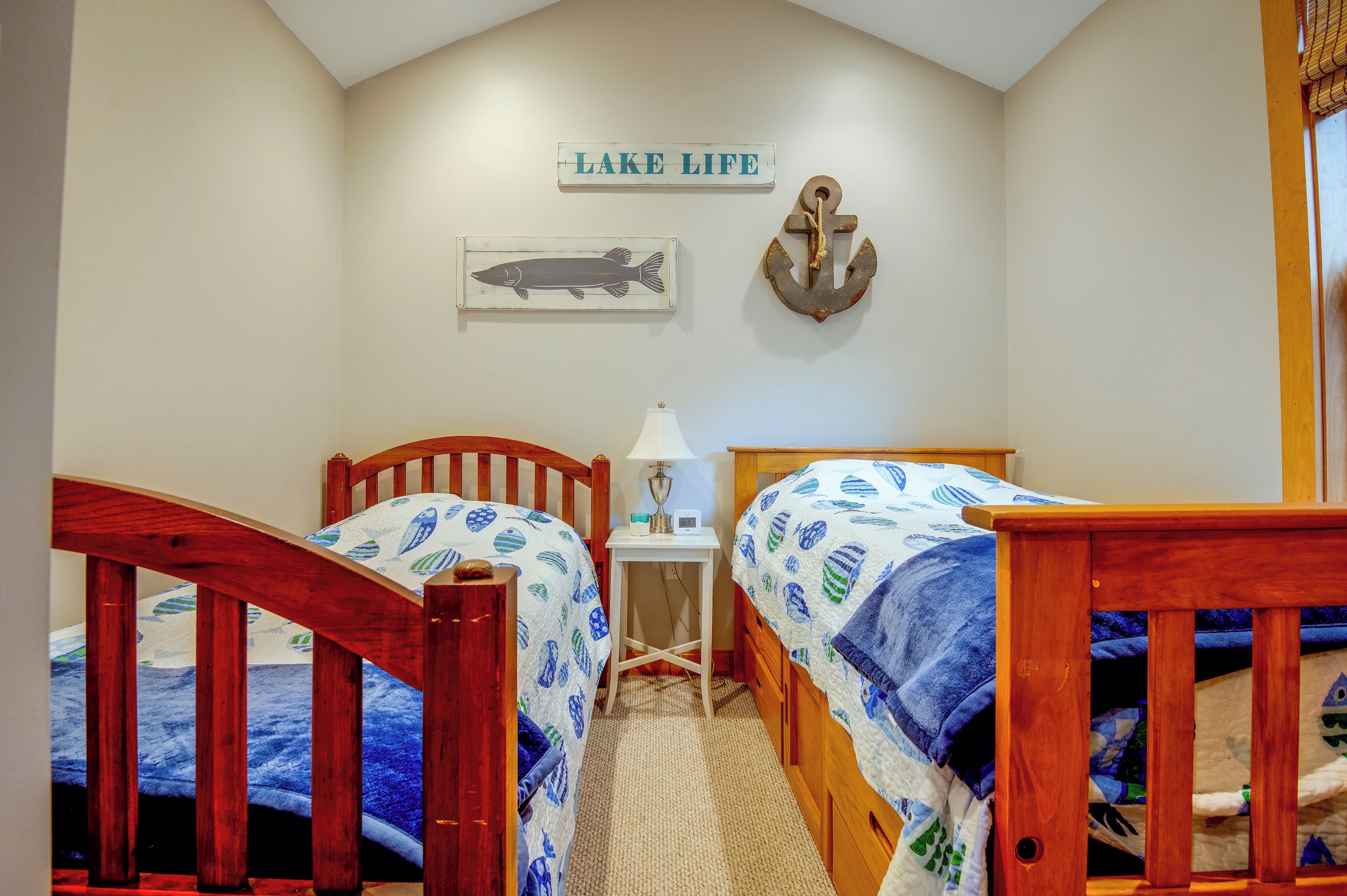 Un dormitorio con dos camas de madera, una mesita de noche, una lámpara, un reloj de pared y un letrero que dice 'LAKE LIFE'.