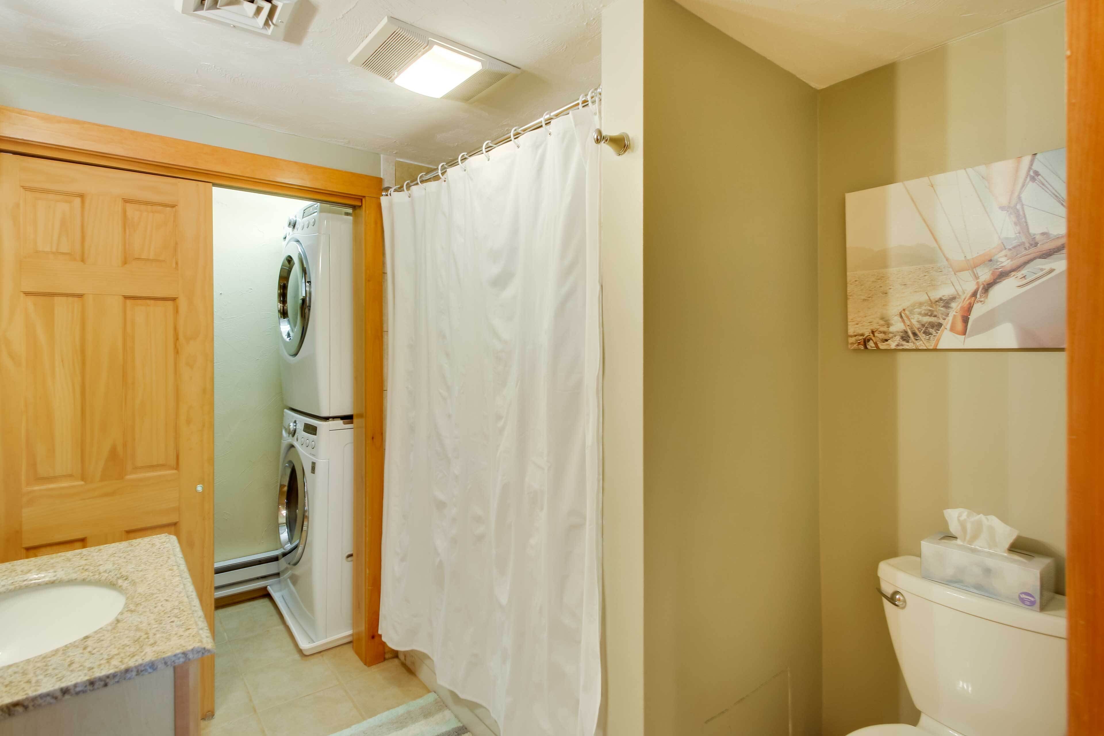 A bathroom with a wooden door, a washing machine, a shower curtain, a toilet, and a painting on the wall.
