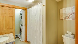 Une salle de bain avec une porte en bois, un lave-linge, un rideau de douche, des toilettes et un tableau accroché au mur.