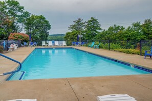 Una piscina rectangular con borde de azulejos azules, rodeada por una terraza de concreto. Hay sillas de descanso y una cerca con vista a un paisaje montañoso.