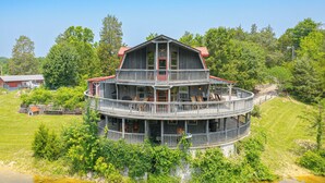 A multi-story waterfront house with balconies, surrounded by greenery and a body of water. - Strawberry Plains Cabin: Private Pond & Game Room! (Kodak)