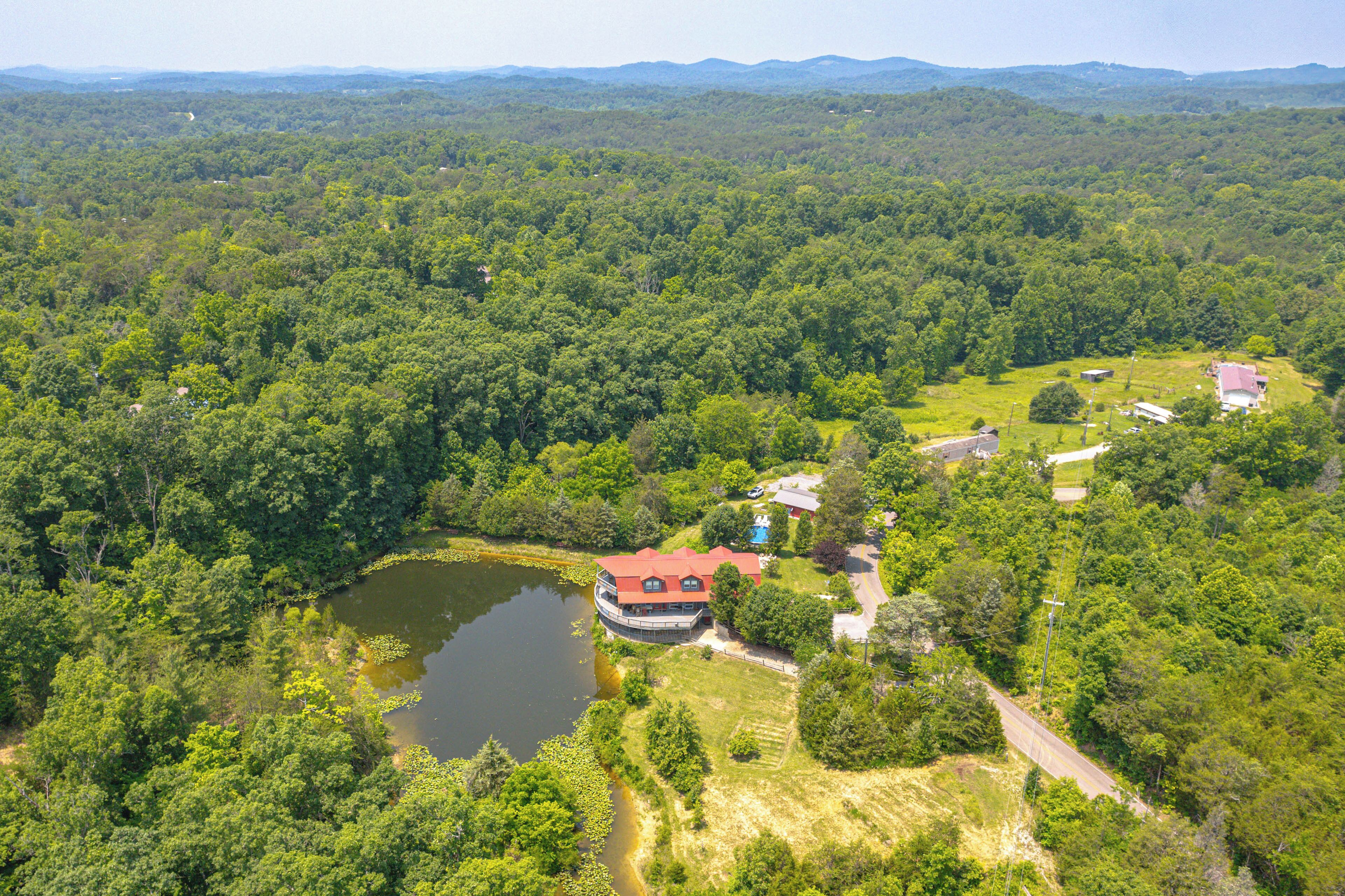 An aerial view of a property with a large lake, dense forest, and a building with a red roof.