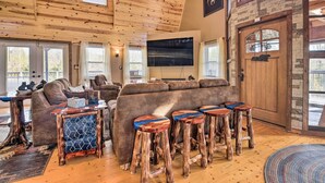 A cozy living room with a wooden ceiling, a large couch, and a TV mounted on the wall. - Strawberry Plains Cabin: Private Pond & Game Room! (Kodak)