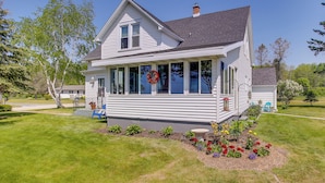 A two-story house with a porch, a front yard with flowers, and a clear blue sky. - 5 Mi to Point Beach State Forest: Home w/ Fire Pit (Two Rivers)