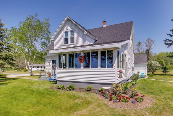 A two-story house with a porch, a front yard with flowers, and a clear blue sky. - 5 Mi to Point Beach State Forest: Home w/ Fire Pit (Two Rivers)