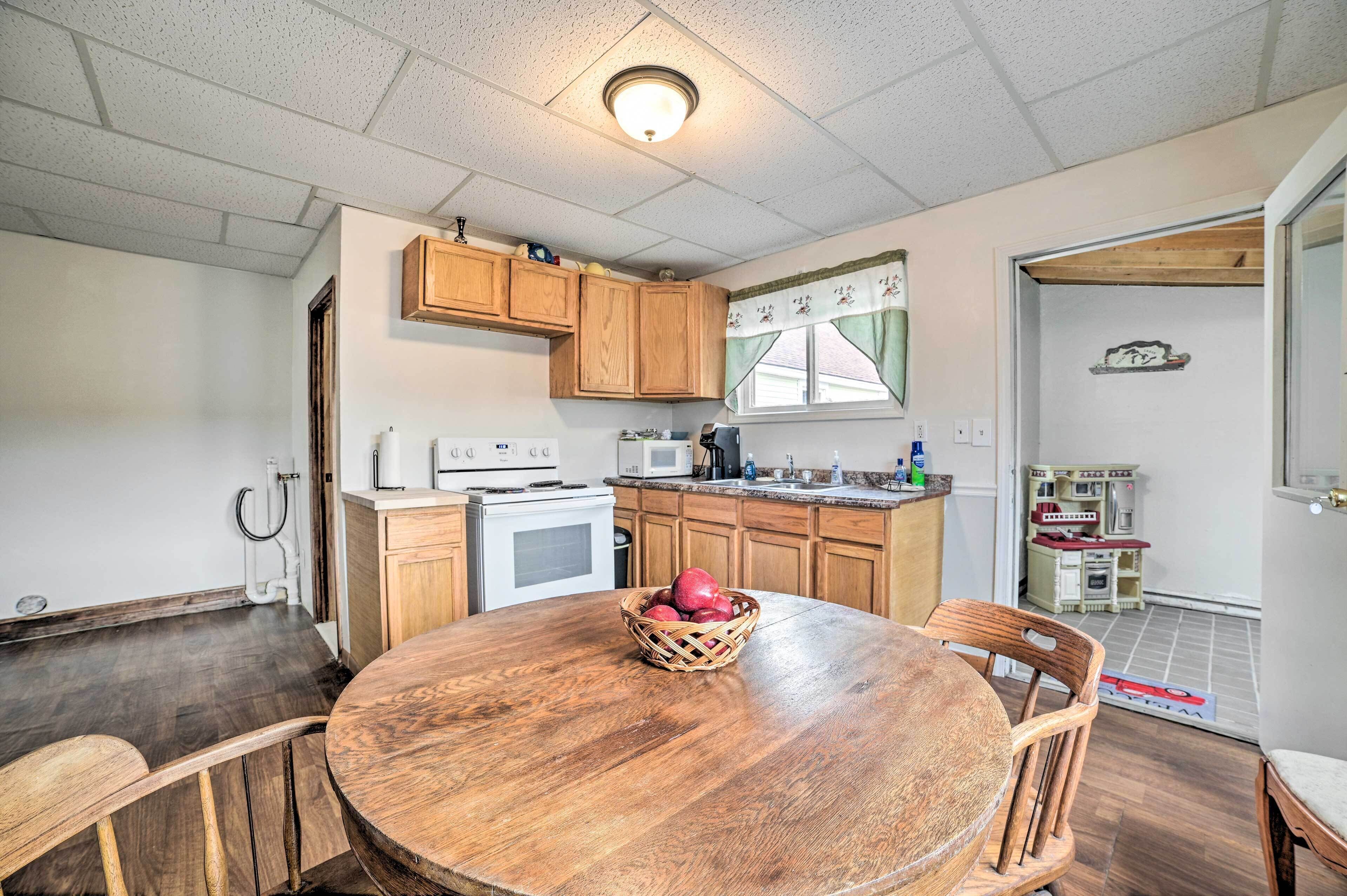 A kitchen with wooden cabinets, a microwave, and a stove. There is a dining table with chairs and a basket of apples.