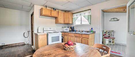 A kitchen with wooden cabinets, a microwave, and a stove. There is a dining table with chairs and a basket of apples.