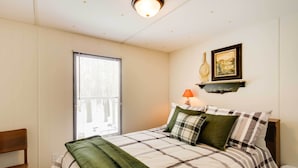 A bedroom with a bed, a chair, a window with blinds, a lamp, and a framed picture on the wall. - Wooded Mcgrath Home w/ Sauna Near Soo Line Trail! (Mc Grath)