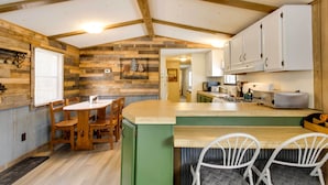 A rustic kitchen with wooden beams, a dining area with a wooden table and chairs, and white cabinets. - Wooded Mcgrath Home w/ Sauna Near Soo Line Trail! (Mc Grath)