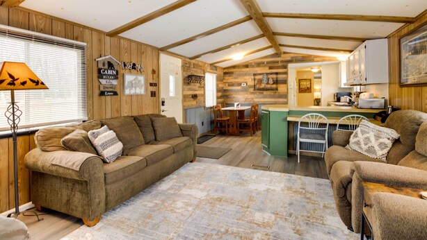 A cozy cabin interior with a wooden ceiling, a sofa, a dining table, and a kitchen area. - Wooded Mcgrath Home w/ Sauna Near Soo Line Trail! (Mc Grath)
