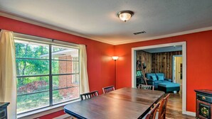 Un coin repas avec une table et des chaises en bois, une grande fenêtre donnant sur un paysage verdoyant et un mur rouge.