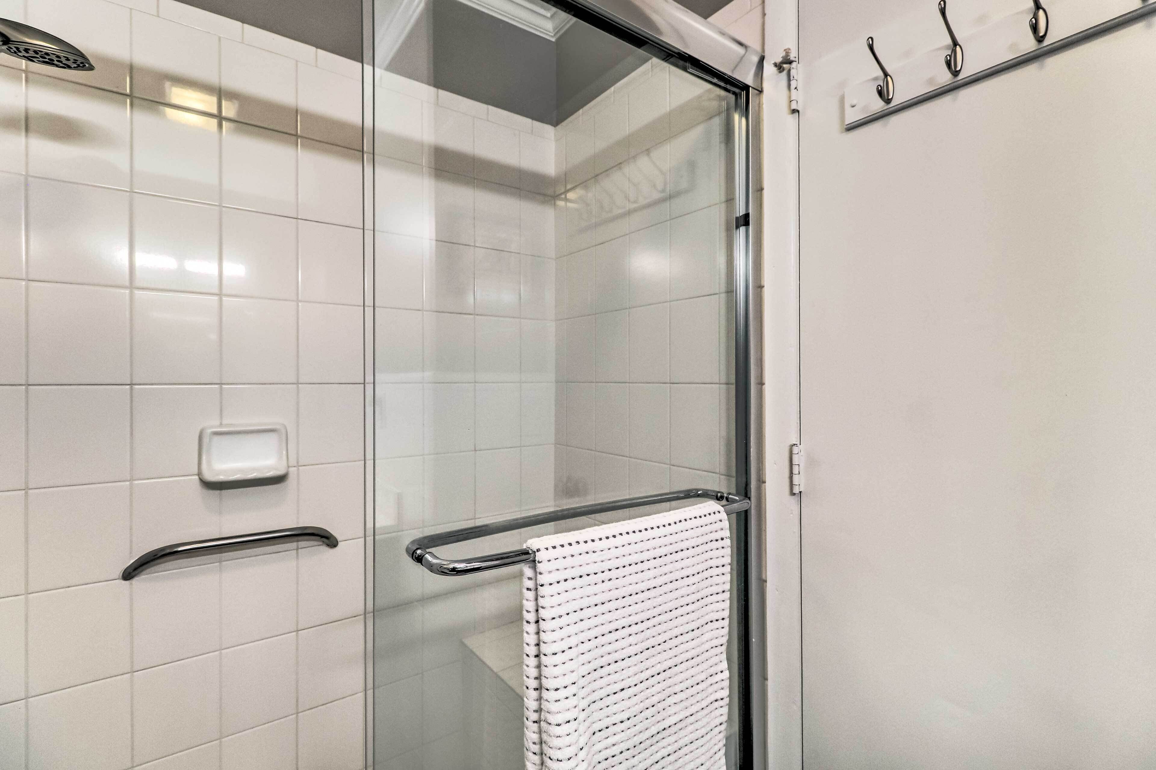 A modern bathroom with a glass shower enclosure, a white towel hanging on a metal towel bar, and a soap dish on the wall.