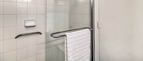 A modern bathroom with a glass shower enclosure, a white towel hanging on a metal towel bar, and a soap dish on the wall.
