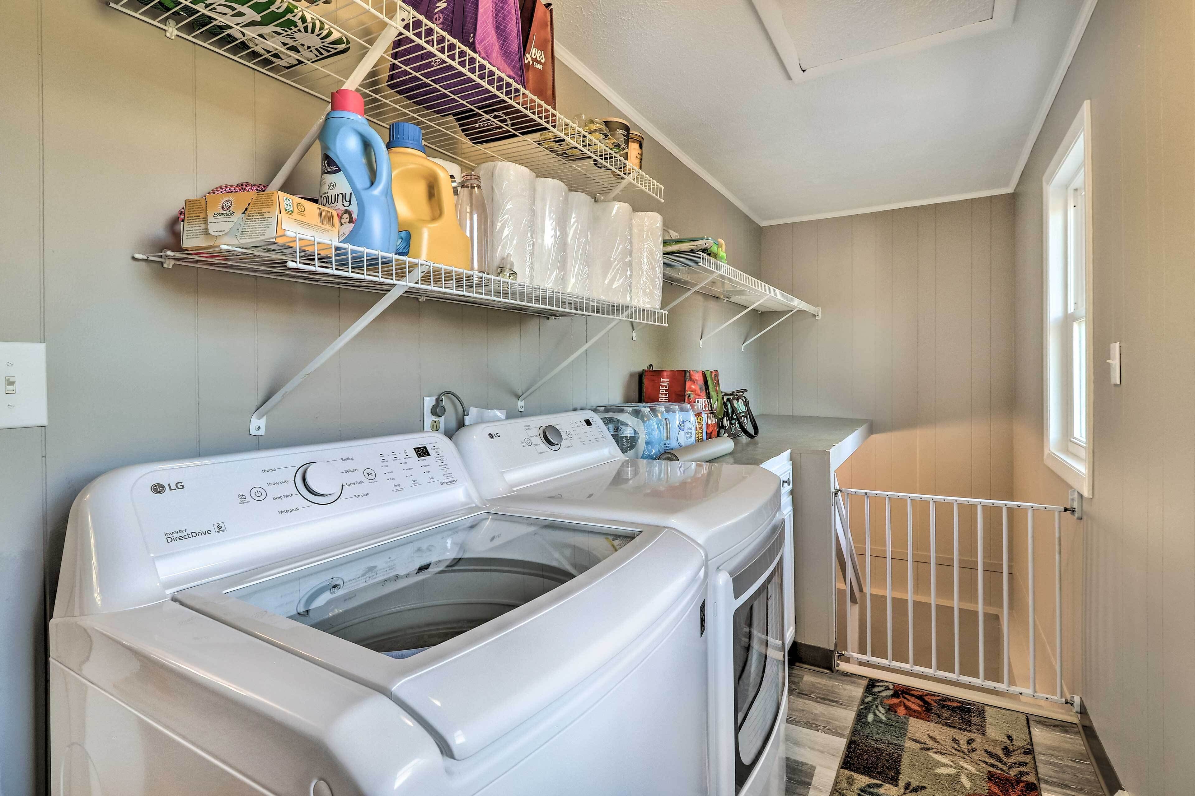 A laundry area with a washing machine, shelves with cleaning supplies, and a baby gate.