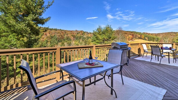 A deck with a table set for two, a grill, and chairs.