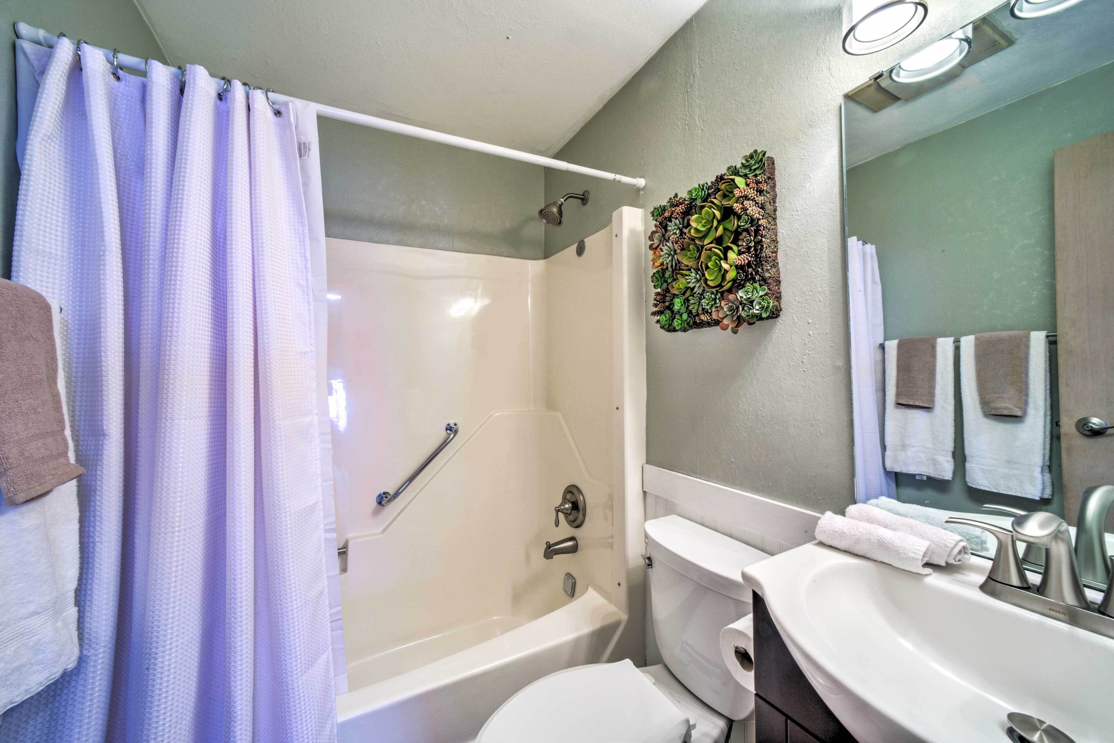 A bathroom with a shower, toilet, sink, and a mirror.