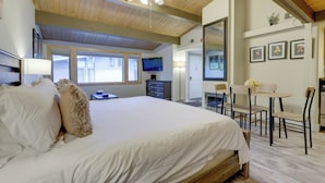 Un dormitorio con una cama grande, vigas de madera en el techo, un ventilador de techo, un televisor en la pared y una zona de comedor con sillas y una mesa.