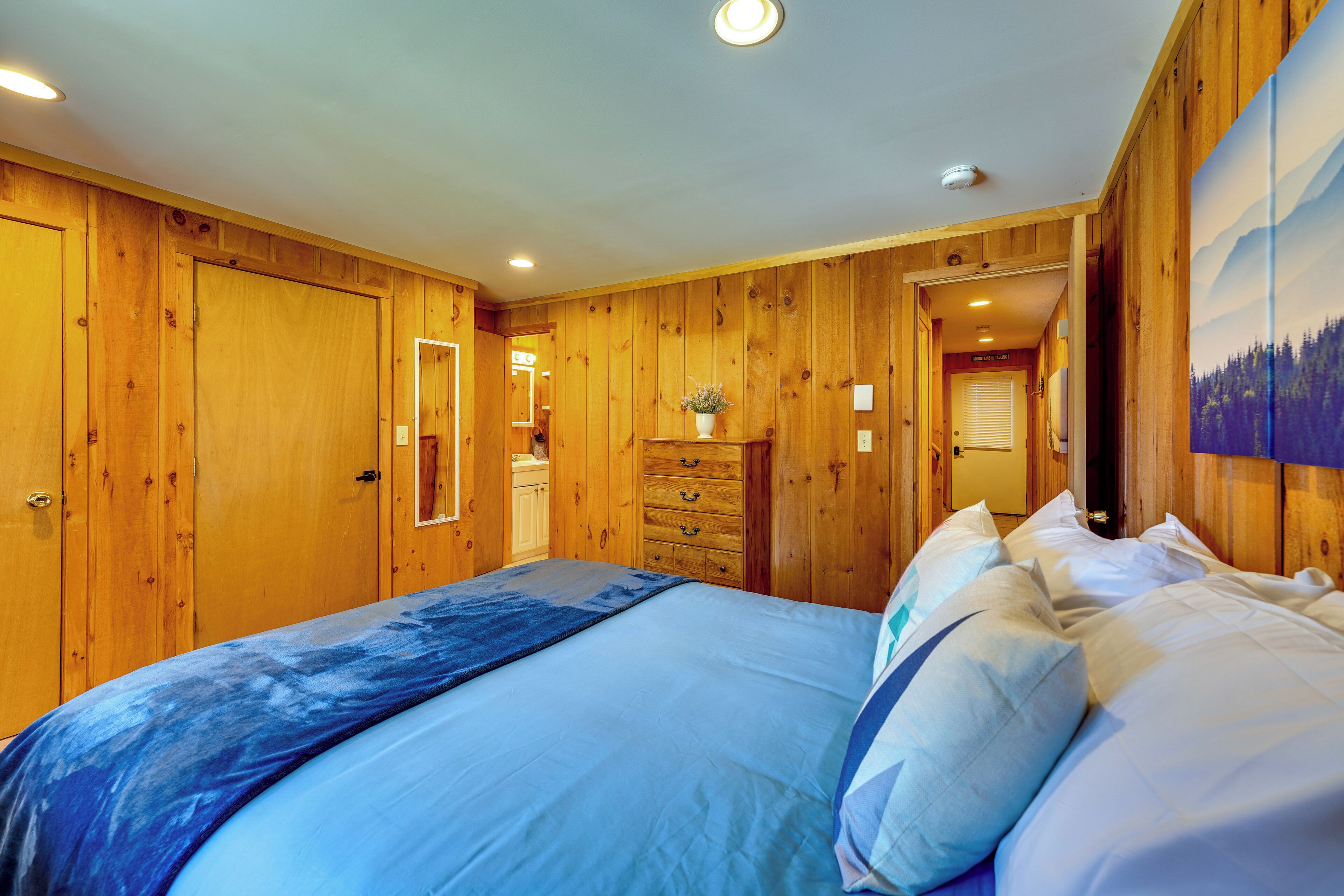 A wooden-paneled bedroom with a bed, dresser, and a painting on the wall.