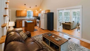 A spacious living room with a brown leather sofa, a wooden coffee table, and a view of the kitchen and dining area. - Waterfront Sebec Lake Home w/ Yard + Fire Pit (Dover-Foxcroft)