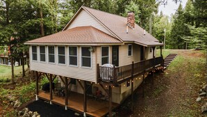 A two-story house with a deck, a chimney, and a covered porch with outdoor seating. - Waterfront Sebec Lake Home w/ Yard + Fire Pit (Dover-Foxcroft)