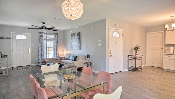 A modern living room with a glass dining table, pink and white chairs, a ceiling fan, and a large window with curtains. - Updated Baton Rouge Home w/ Grill ~ 10 Mi to Dtwn! (Baton Rouge)