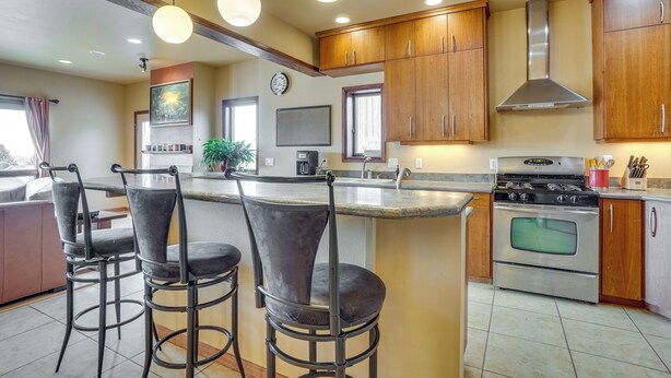 A modern kitchen with a central island, bar stools, wooden cabinets, stainless steel appliances, and pendant lighting. - Upscale Laramie Home w/ Hot Tub & Patio! (Laramie)