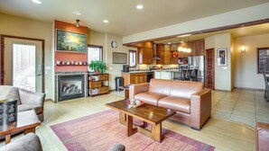A spacious living room with a fireplace, a sofa, a coffee table, and a kitchen area with wooden cabinets and a dining table. - Upscale Laramie Home w/ Hot Tub & Patio! (Laramie)