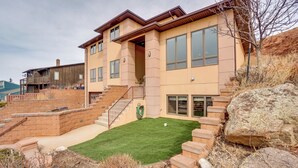 A two-story house with a green lawn, stone steps, and a large rock. - Upscale Laramie Home w/ Hot Tub & Patio! (Laramie)