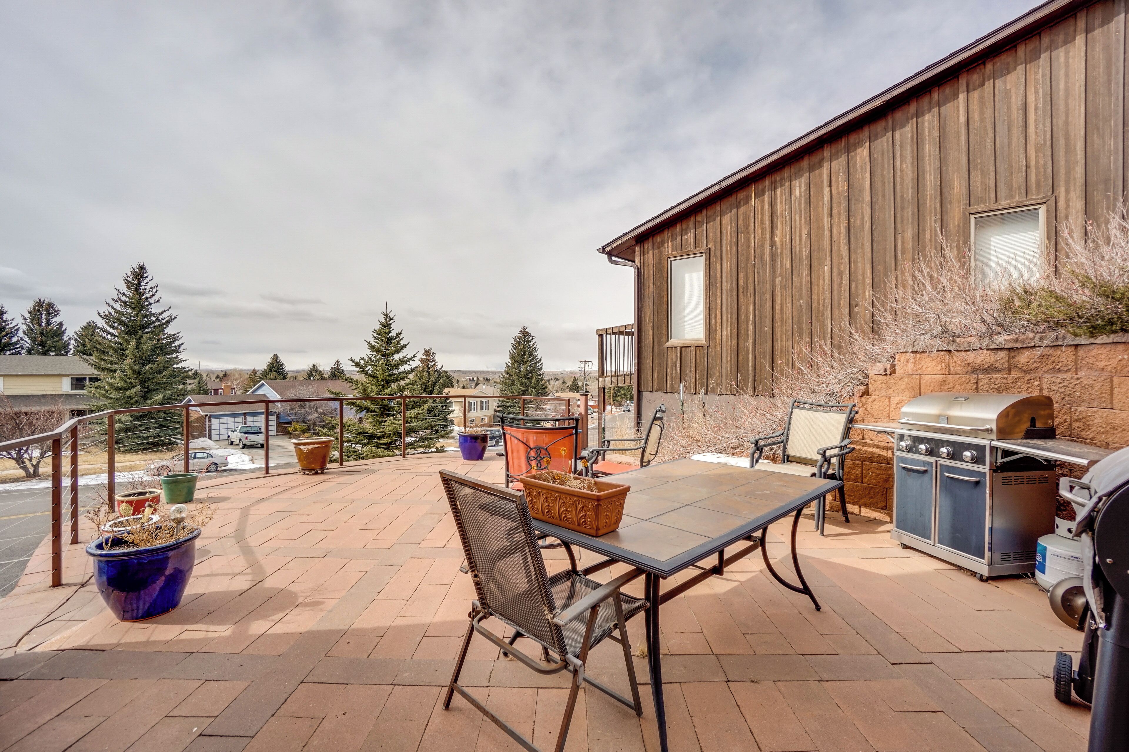 An outdoor patio with a table and chairs, a barbecue grill, and potted plants.