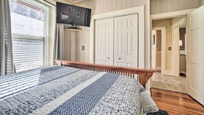 A bedroom with a bed, a television mounted on the wall, and a closet with white doors. - Quaint Home w/ Porch in Downtown Waynesville! (Waynesville)