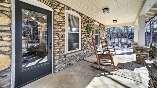 A stone exterior with a black door, a covered porch with a rocking chair, and a view of a snowy landscape. - Quaint Home w/ Porch in Downtown Waynesville! (Waynesville)