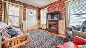 A living room with a fireplace, leather sofas, a TV, and patterned wallpaper. - Quaint Home w/ Porch in Downtown Waynesville! (Waynesville)