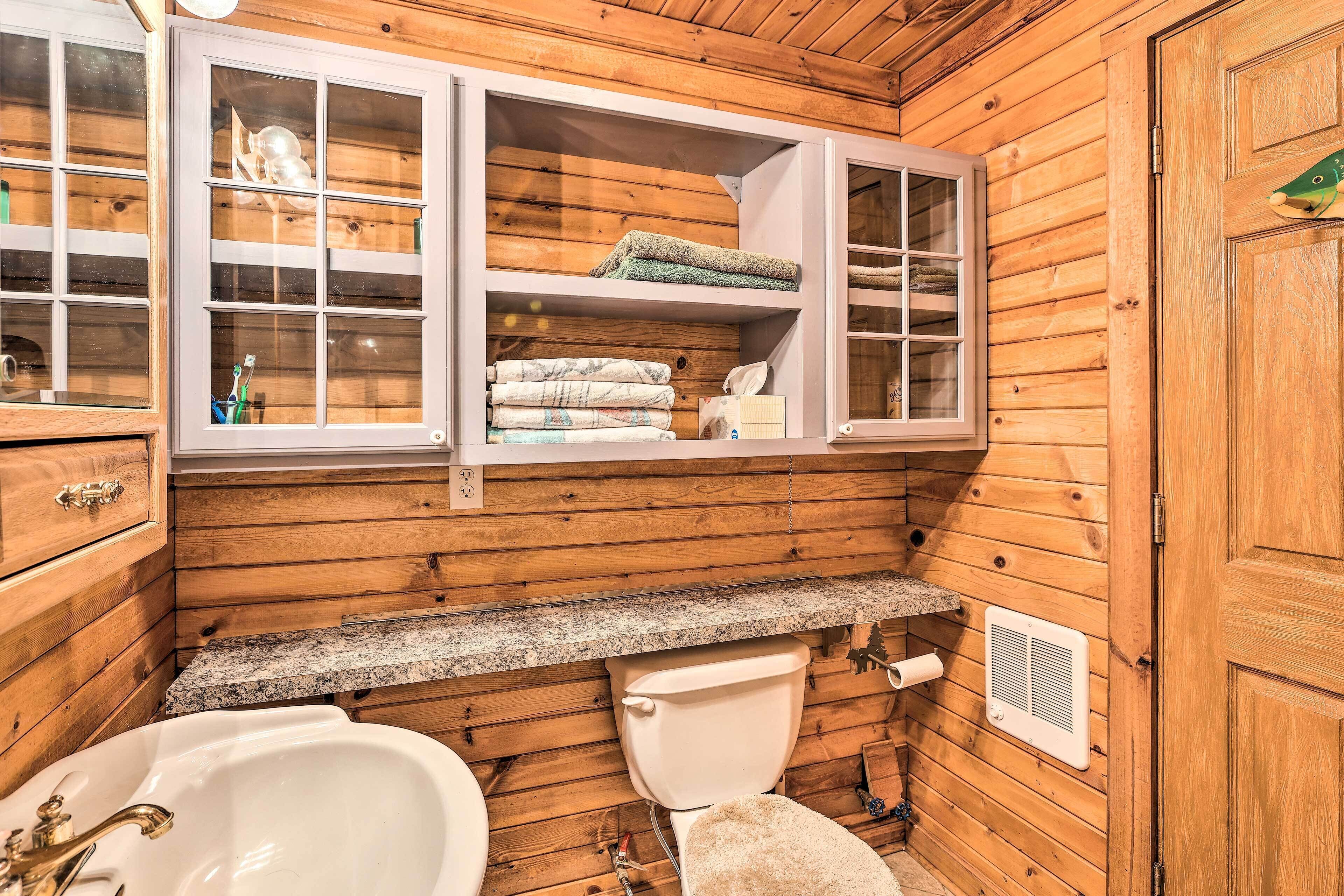Baño de cabaña de madera con lavabo, inodoro y repisas abiertas sobre el inodoro.