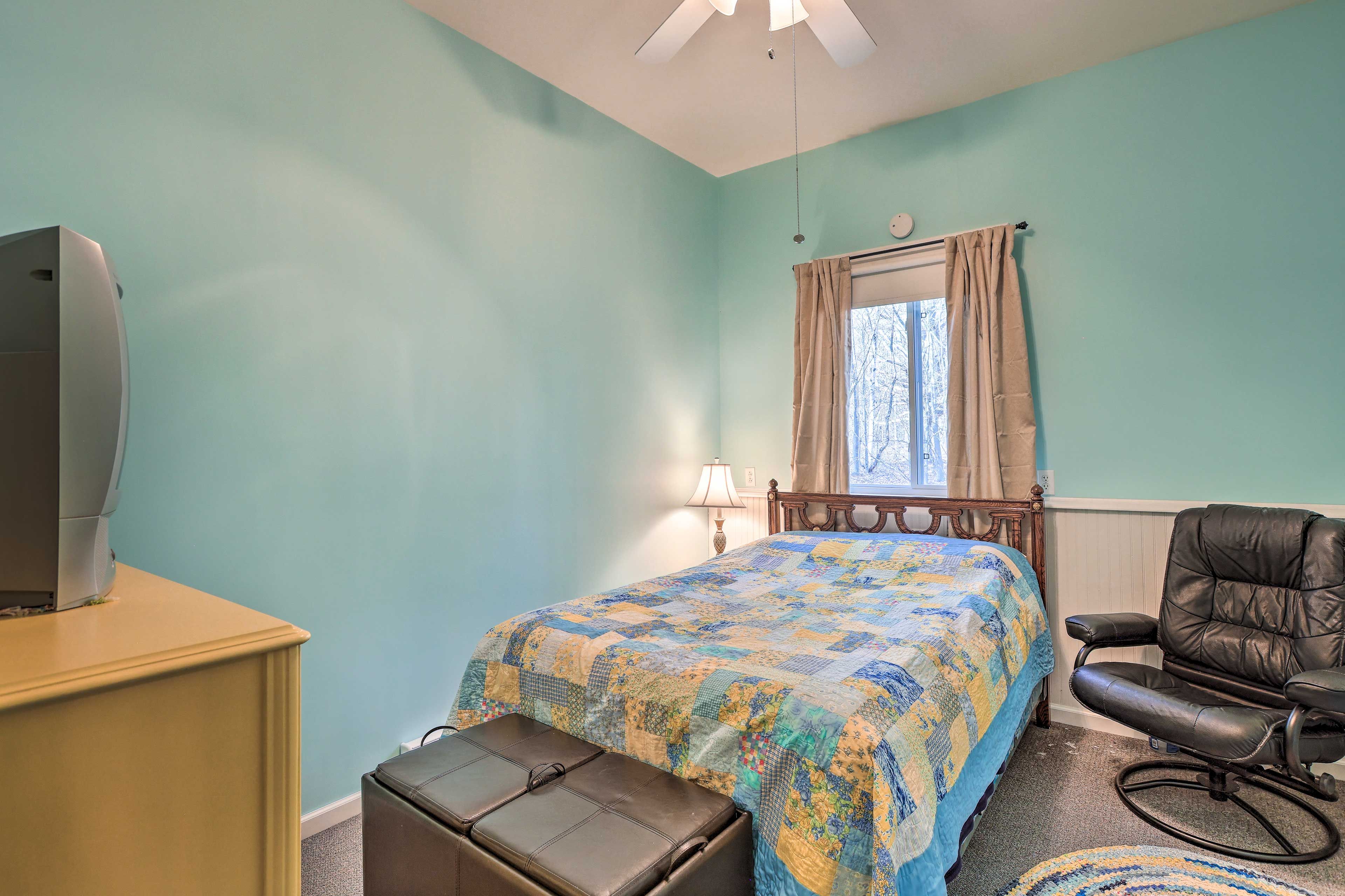 A bedroom with a bed, a chair, a desk, and a window with curtains.