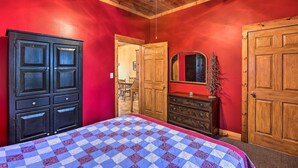 Una habitación con pared roja, techo de madera, cama con colcha a cuadros, cómoda y una puerta.