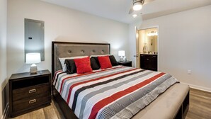 A bedroom with a large bed, a nightstand with drawers, a ceiling fan, and a bathroom visible through an open door. - Pet-friendly Home: Spacious Yard + Community Perks (Montross)