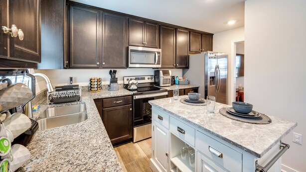 A modern kitchen with dark wood cabinets, stainless steel appliances, granite countertops, and a built-in oven. - Pet-friendly Home: Spacious Yard + Community Perks (Montross)
