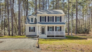 A two-story house with a porch, surrounded by a forest. - Pet-friendly Home: Spacious Yard + Community Perks (Montross)