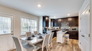 A modern kitchen with dark cabinets, a stainless steel microwave, and a dining area with a marble table and grey chairs. - Pet-friendly Home: Spacious Yard + Community Perks (Montross)