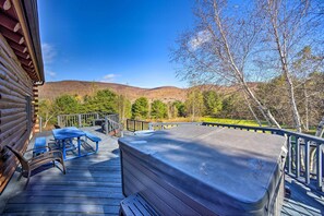 A wooden deck with picnic tables and a hot tub. - Pet-friendly New York Cabin w/ Hot Tub & Game Room (Maplecrest)