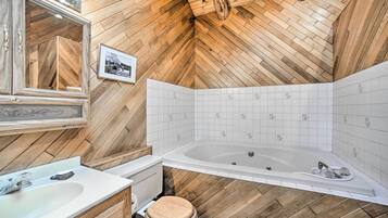 Un baño con paredes de madera, una bañera grande, un lavamanos y un inodoro.
