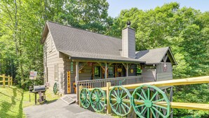 A rustic cabin with a porch, large green wheels, and a chimney.