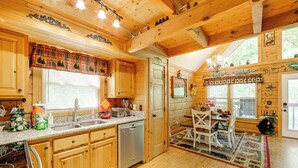A wooden cabin kitchen with a granite countertop, wooden cabinets, a dishwasher, and a dining area with a table and chairs.