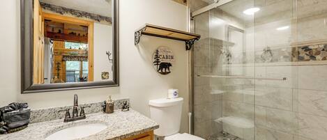 A bathroom with a sink, mirror, toilet, and shower.