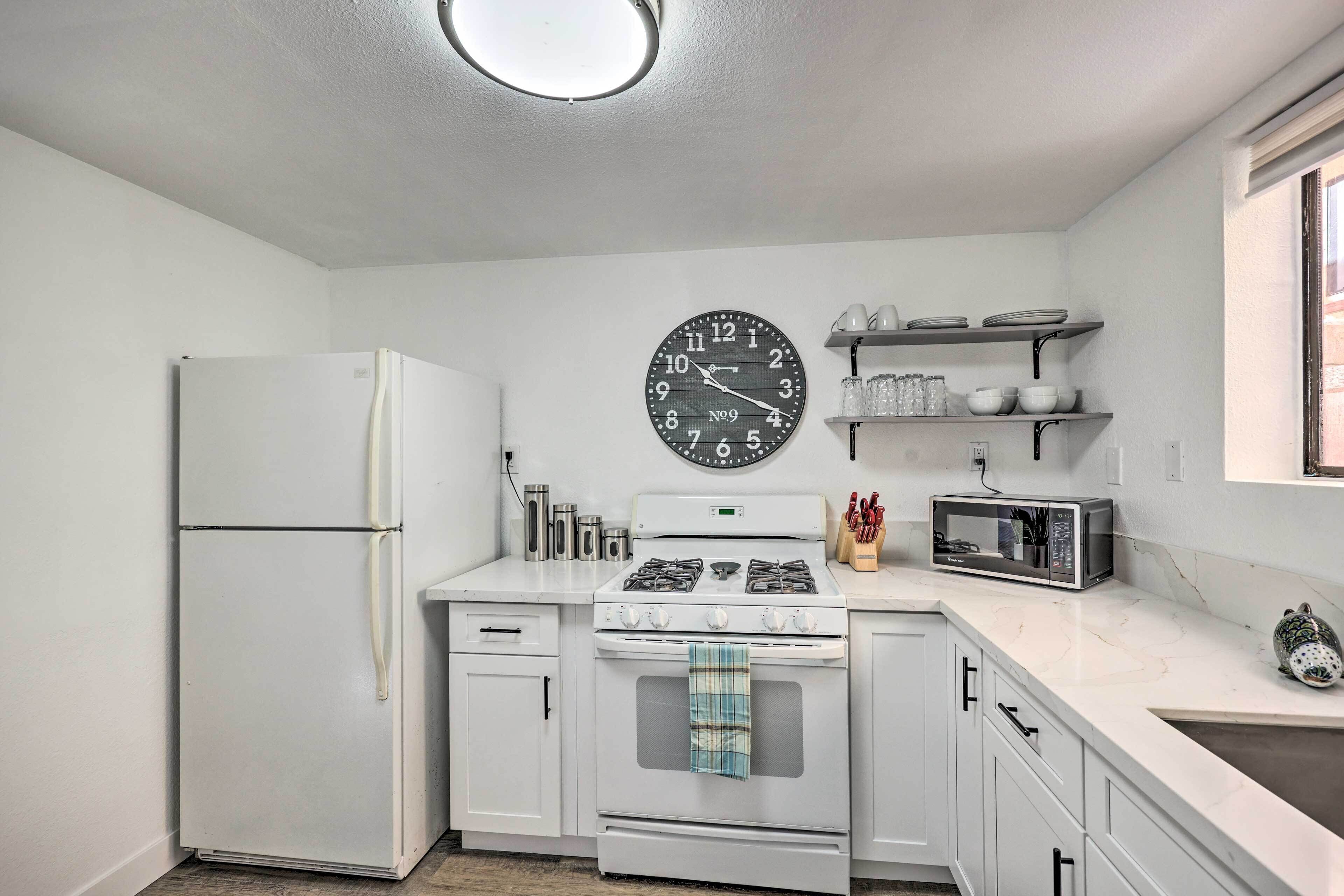 Une cuisine de taille réduite, avec des appareils électroménagers blancs, une horloge et un four à micro-ondes.