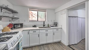 A kitchen with white cabinets, a stove, a microwave, and a window. - Oxnard Apartment < 1/2 Mi to Beaches! (Oxnard)
