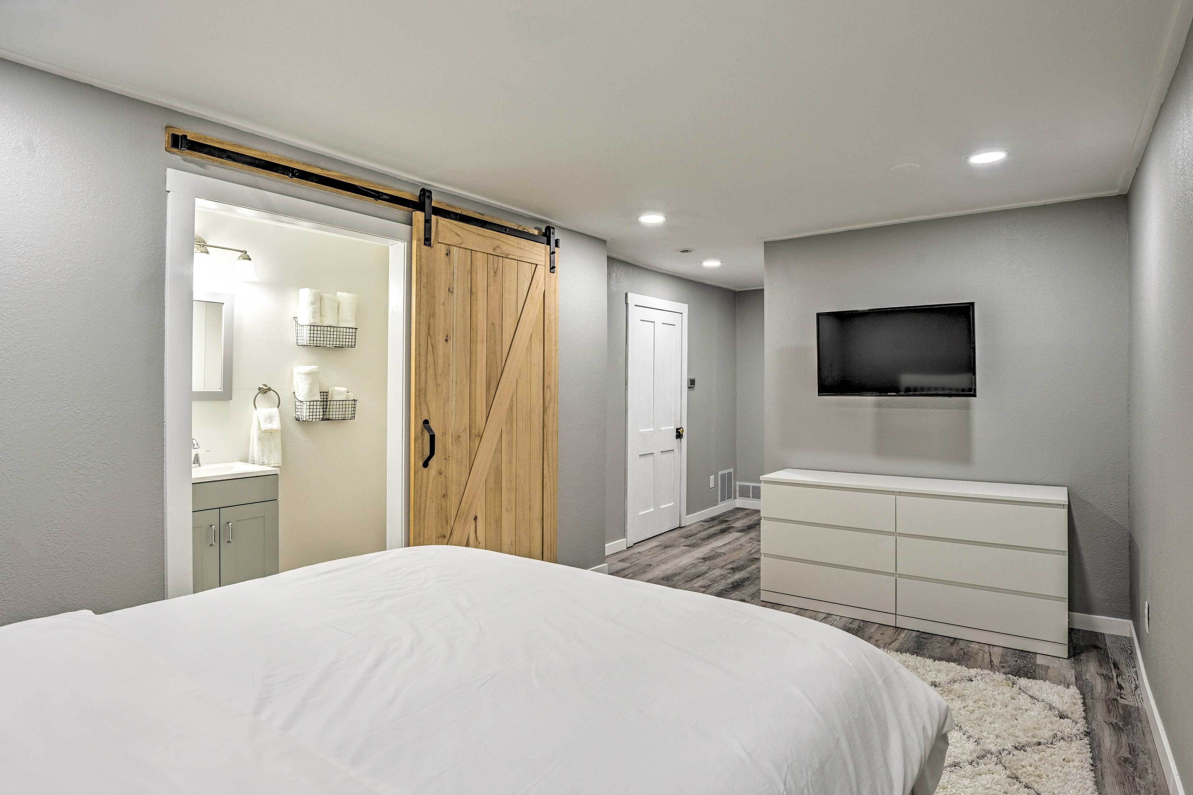 A bedroom with a bed, a sliding door, a dresser, a television, and a bathroom visible through the door.