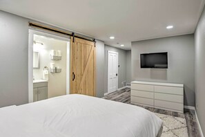 Una camera da letto con un letto, una porta scorrevole, una cassettiera, una televisione e un bagno visibile attraverso la porta.