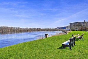 Vista sul fiume con una zona verde, un edificio in pietra e una panchina.